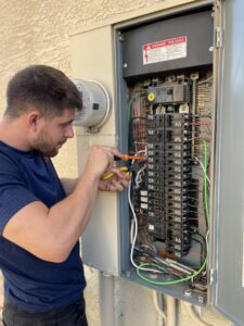 An electrician performing work inside an outdoor electrical panel with tools for Miller and Sons Electric in North Myrtle Beach, SC.