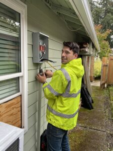An electrician using a drill to work on an outdoor electrical service panel for OutToday Electrical, Heating, Plumbing, and Air in Bellevue, WA