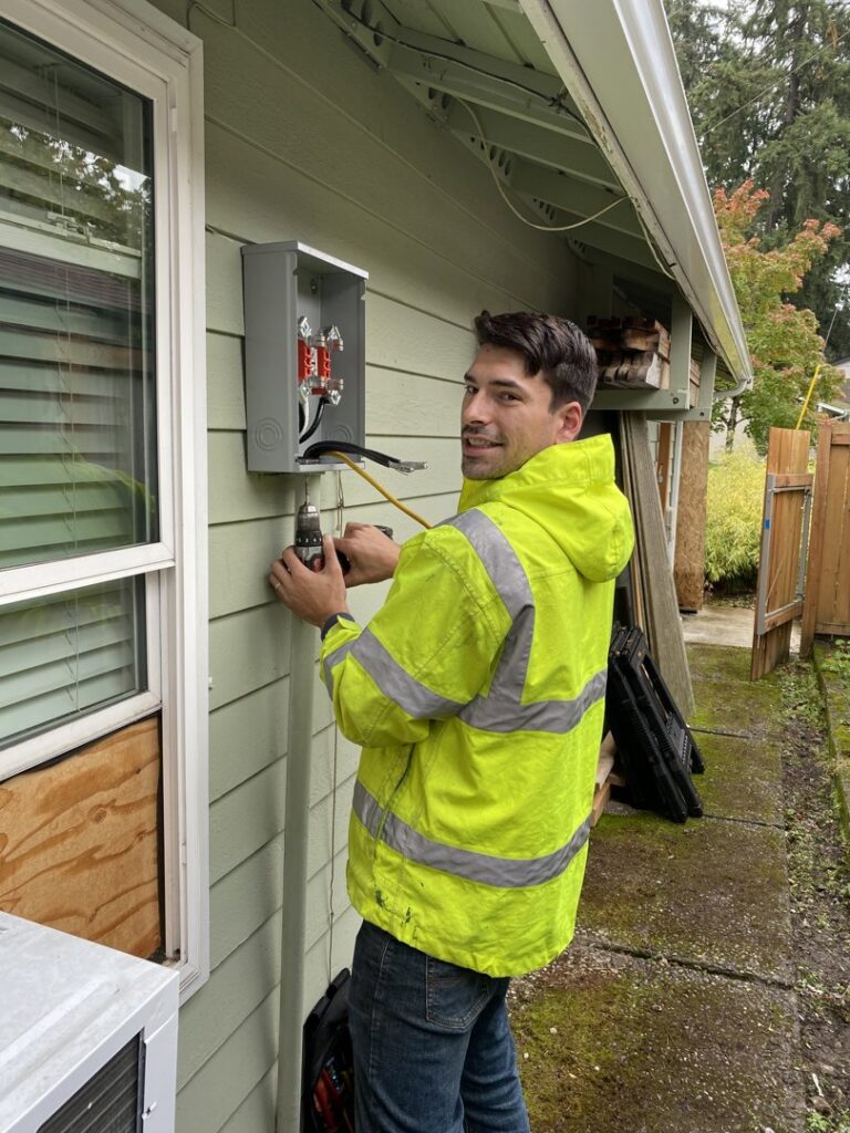 An electrician using a drill to work on an outdoor electrical service panel for OutToday Electrical, Heating, Plumbing, and Air in Bellevue, WA