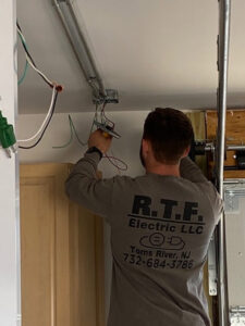 An electrician from RTF Electric LLC working on overhead wiring and conduit installation in Toms River, NJ.
