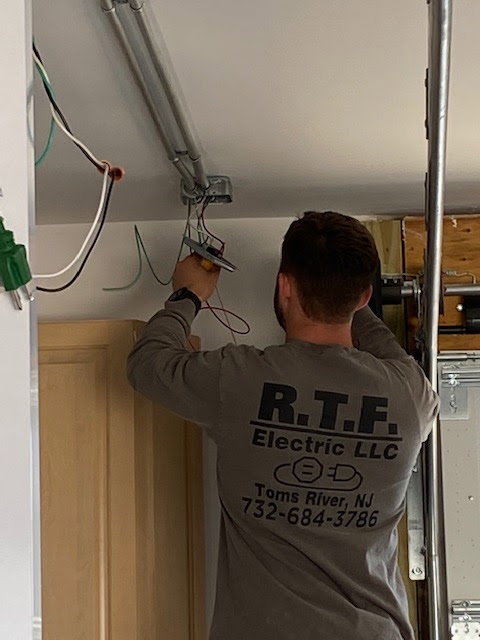 An electrician from RTF Electric LLC working on overhead wiring and conduit installation in Toms River, NJ.