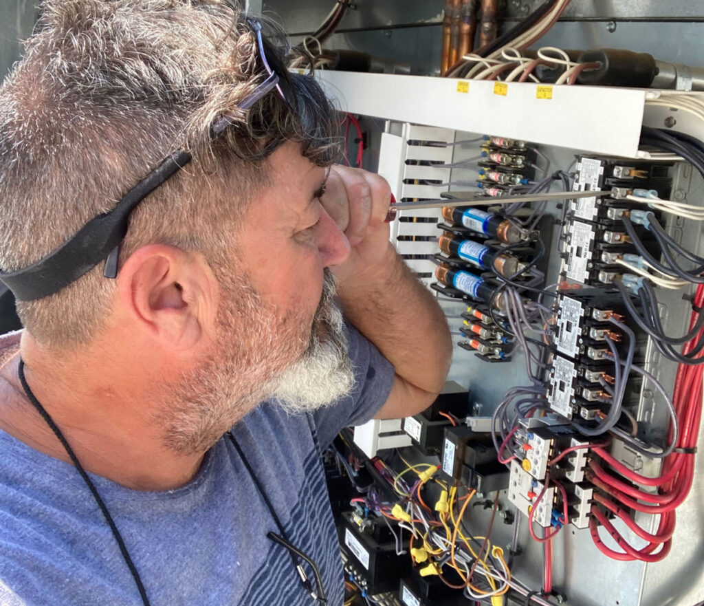 An electrician working on an open electrical control panel with a screwdriver for Ace Electric Inc. in Valdosta, GA.