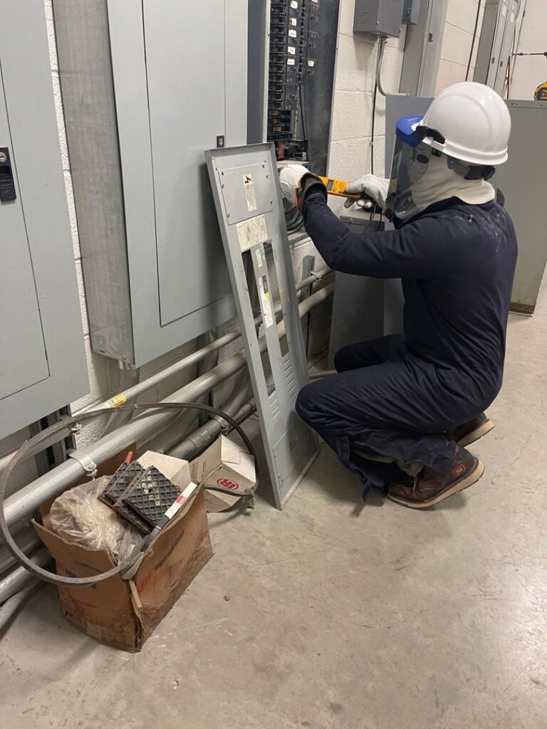 An electrician in full safety gear working on an electrical panel for AVA Electric, LLC in Fort Worth, TX.