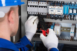 An electrician in a hard hat and gloves working on an electrical panel for Faith Electrical Service in Billings, MT.