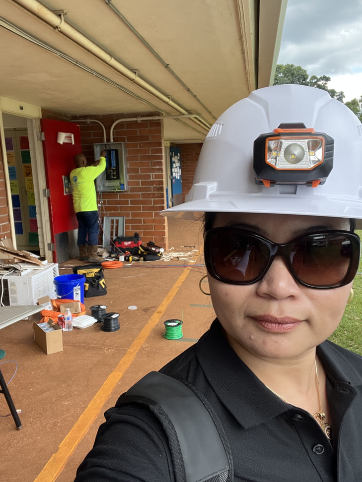 An electrician working on an outdoor electrical panel, with a colleague in the foreground, representing Mcdaniel Electric, LLC in Waipahu, HI.
