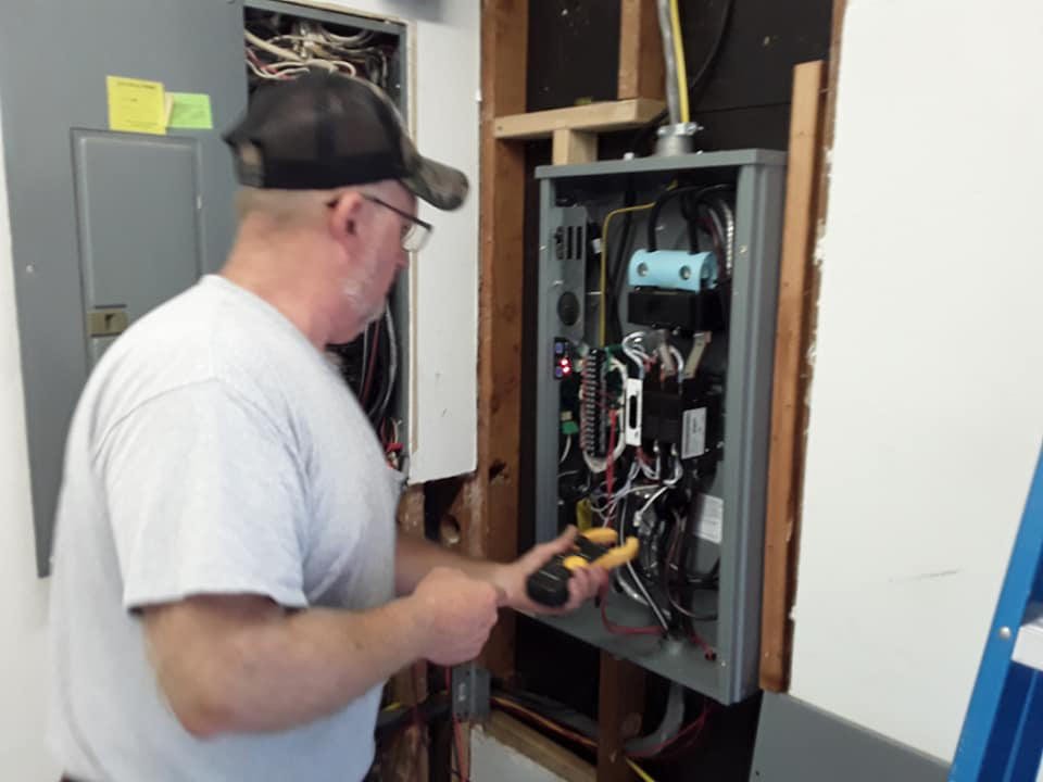 An electrician using a multimeter to work on an open electrical panel for Bluegrass Power & Electric in Lexington, KY.