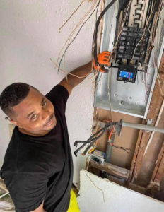 An electrician wearing gloves working on an exposed electrical panel with many wires for Plug It In Electric & more in Kansas City, MO.