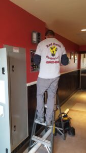An electrician from Red Earth Electric LLC on a ladder working on an electrical panel in Oklahoma City, OK.