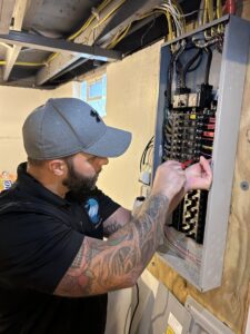 An electrician from Surge Electric LLC working on an open electrical panel, connecting wires in Youngstown, OH.