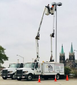 An electrician from TCL Electrical and Lighting working on a tall parking lot light pole in North Aurora, IL