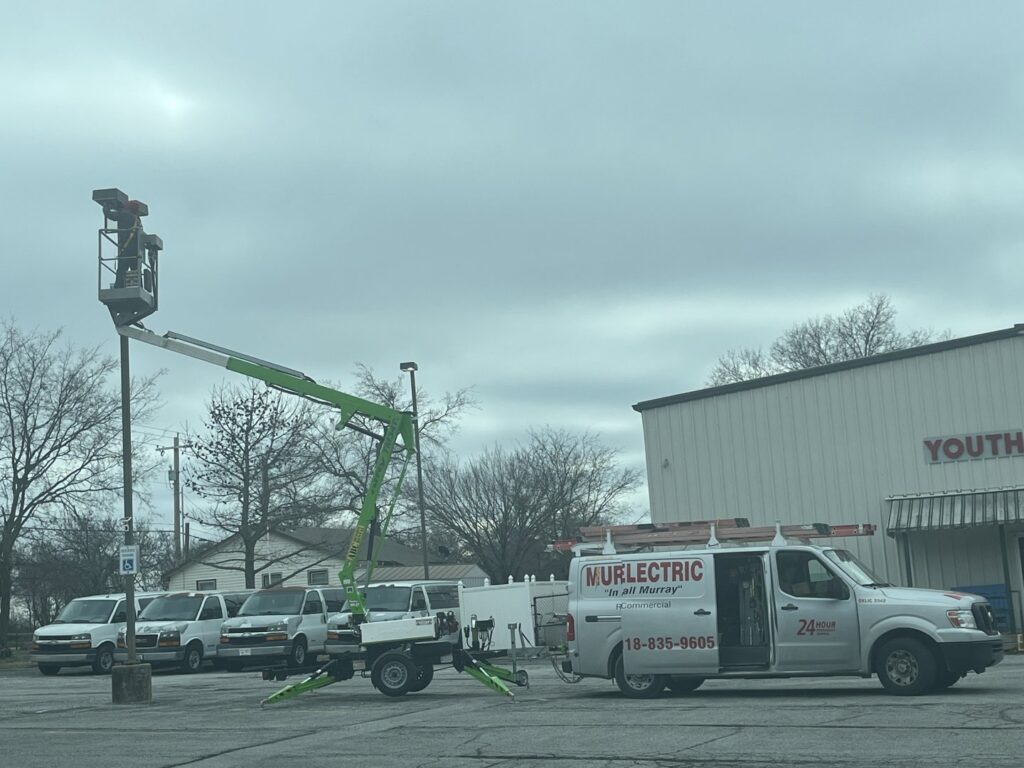 An electrician from Murray Electric & Plumbing working on a pole-mounted light fixture using a bucket lift in Broken Arrow, OK.