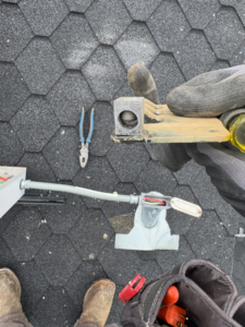 An electrician's gloved hand working on an electrical component on a shingled roof for Garcia Electric Services in Bonita, CA.