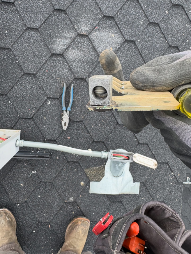 An electrician's gloved hand working on an electrical component on a shingled roof for Garcia Electric Services in Bonita, CA.