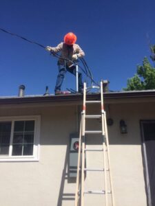An electrician on a roof working on service entrance wiring for a residential property, provided by JJRS Electrical, LLC in Colorado Springs, CO.