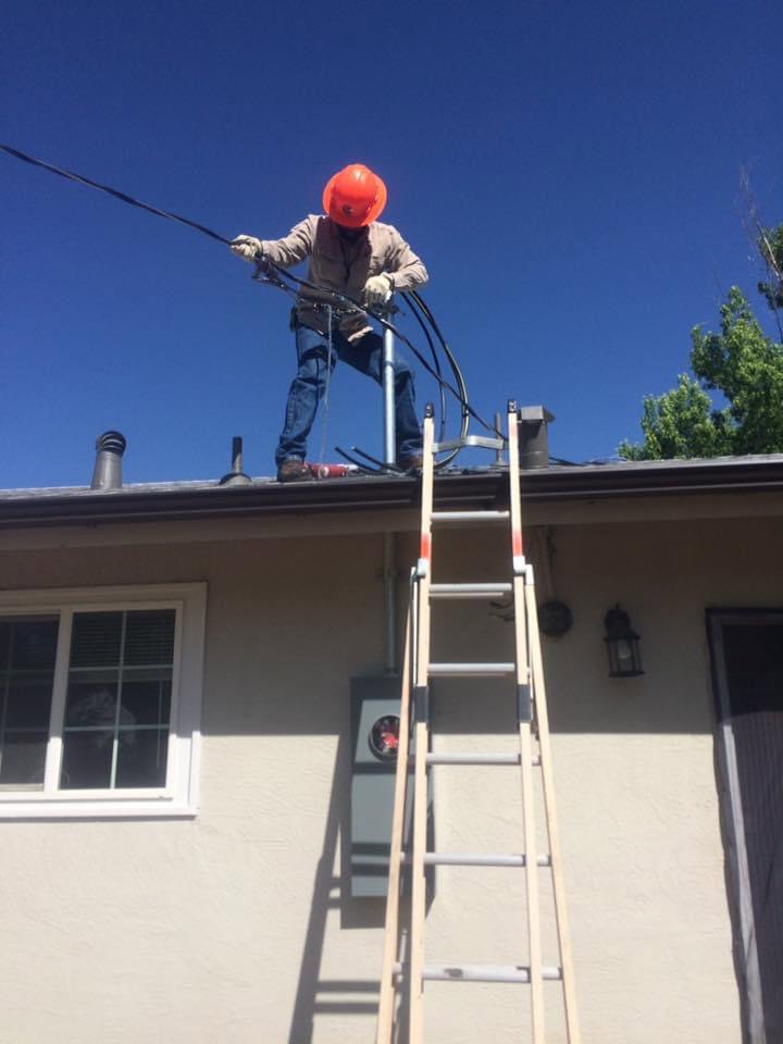 An electrician on a roof working on service entrance wiring for a residential property, provided by JJRS Electrical, LLC in Colorado Springs, CO.