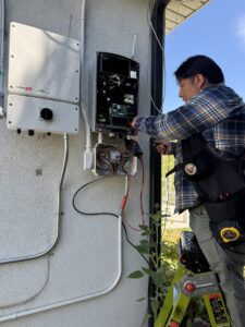 An electrician working on an outdoor solar inverter with a multimeter for Pioneer Electric LLC in West Valley City, UT.