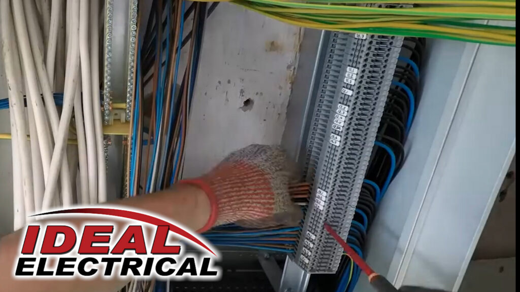 An electrician from Ideal Services NW in Fife, WA, working on a terminal block with multiple wires in an electrical panel.