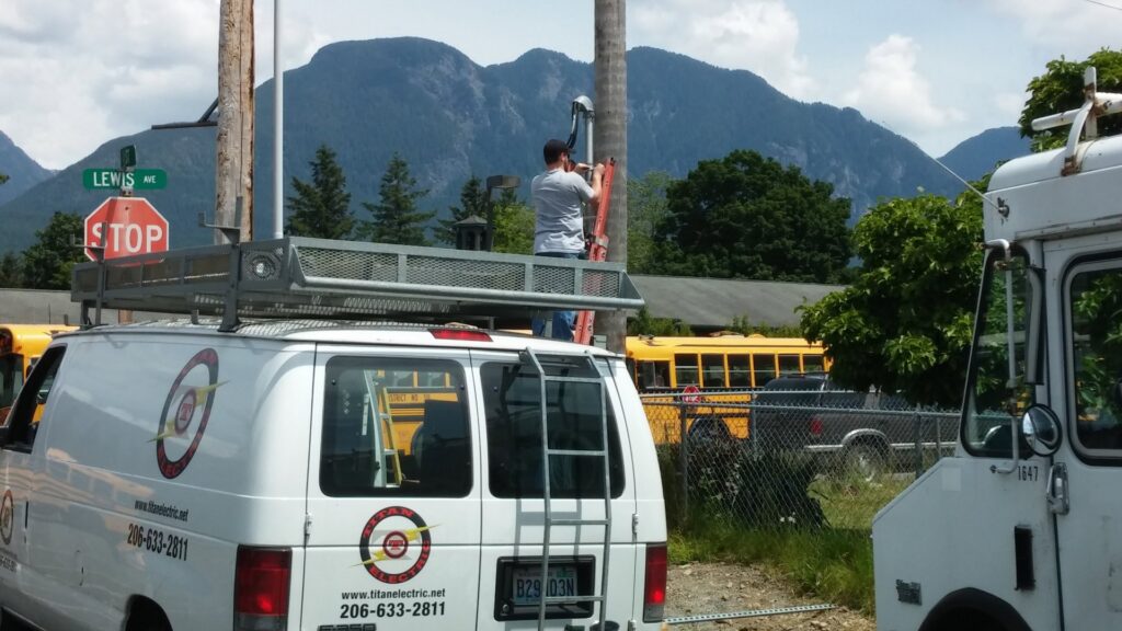An electrician from Titan Electric working on a utility pole next to a company van in Bellevue, WA.