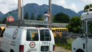 An electrician from Titan Electric working on a utility pole next to a company van in Bellevue, WA.
