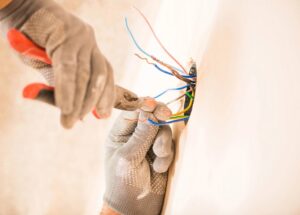An electrician wearing gloves working on colorful electrical wires coming out of a wall for J3 Services in Goose Creek, SC.