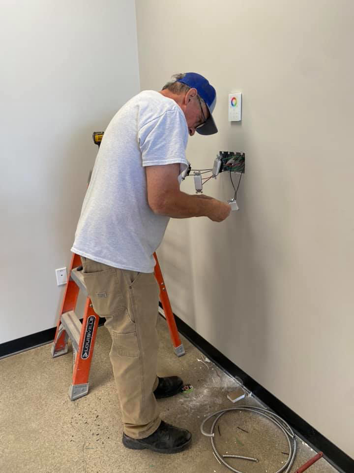 An electrician on a ladder installing or repairing electrical wiring in a wall box for Frederick Electric in Phoenix, AZ.