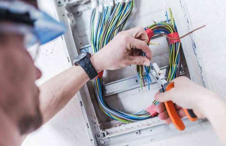 Electrician's hands working on a wiring panel, stripping and connecting colorful wires with pliers for D & D Cabling Solutions in Arlington, TX.