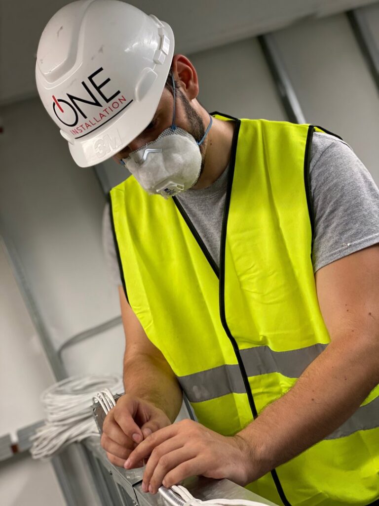 An electrician from One Installation Inc. working on a wiring project in Davie, FL, wearing a hard hat and safety vest