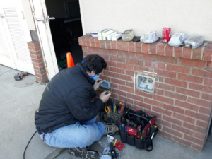 An electrician from Brooker Electric in Roswell, GA, working on an outdoor electrical outlet on a brick wall with tools nearby.