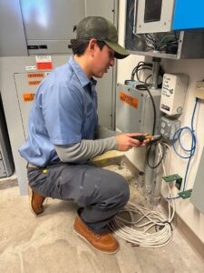 An electrician working on wiring near electrical panels with a "Danger High Voltage" sign at Three Rivers Electric in Fort Wayne, IN.