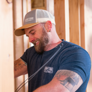 A smiling electrician working with electrical wires in a framed wall for Hometown Electric in Delta, CO.