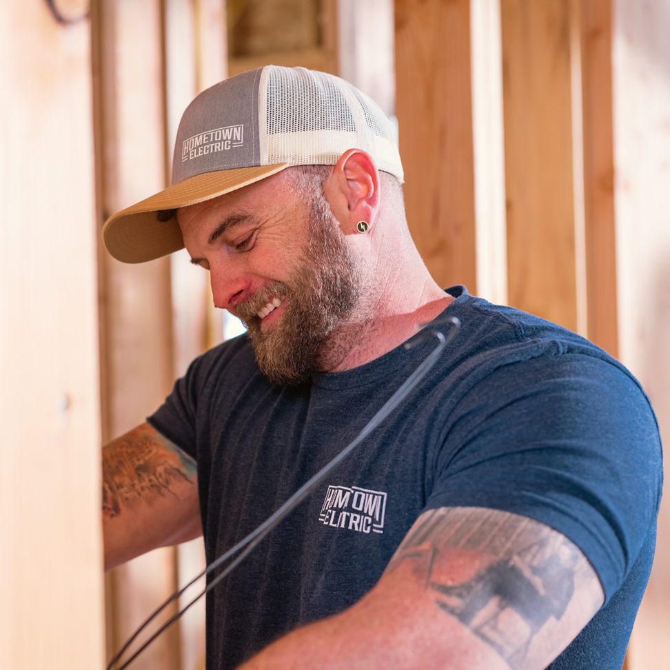 A smiling electrician working with electrical wires in a framed wall for Hometown Electric in Delta, CO.