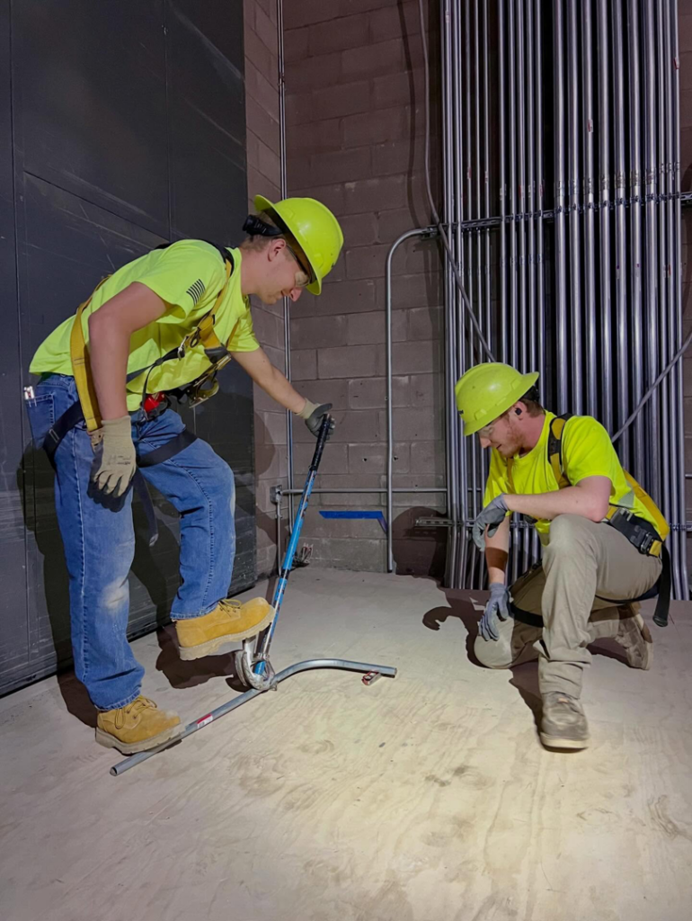 Two electricians in hard hats bending electrical conduit on a job site for Votaw Electric in Fort Wayne, IN