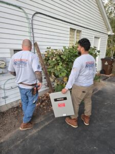 Two electricians from National Electric - Lansing carrying a Generac electrical panel in Lansing, MI.