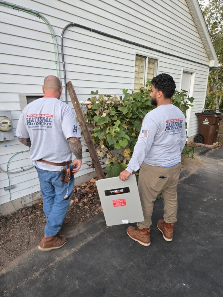 Two electricians from National Electric - Lansing carrying a Generac electrical panel in Lansing, MI.
