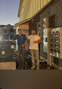 Two electricians next to commercial electrical panels on a construction site, performing installation for JL's Electric Inc. in Norman, OK.
