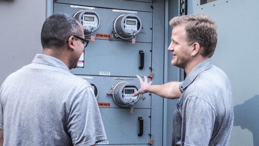 Efficient Electric electricians discussing readings on electrical meters at a service panel in Canton, MI.