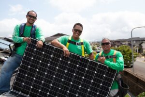 Three electricians from Alternate Energy Inc. holding a solar panel during installation in Pearl City, HI.