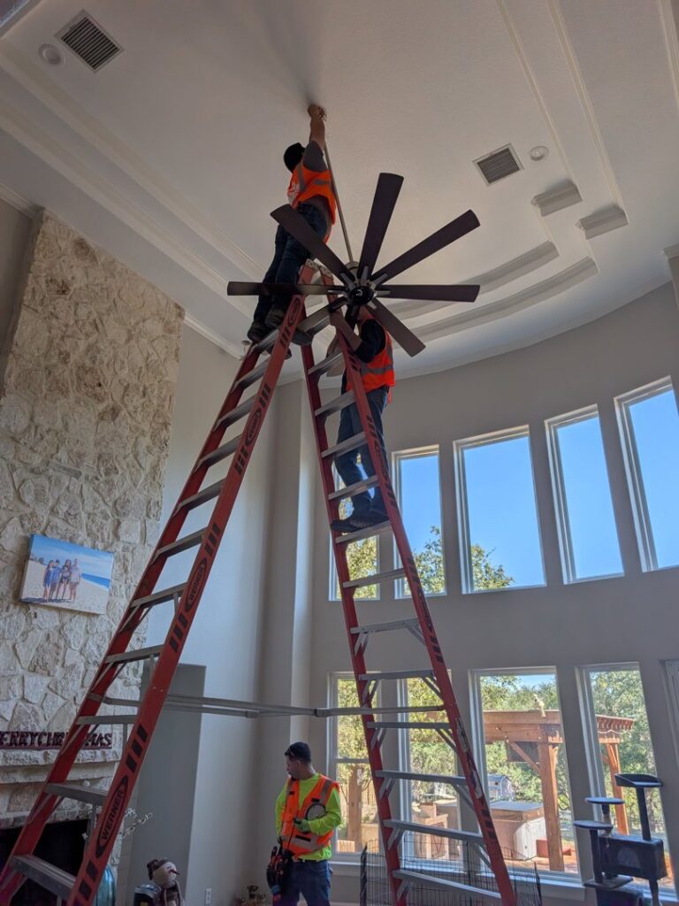 Electricians from Mario Electric installing a large ceiling fan in a high-ceiling room in San Antonio, TX.