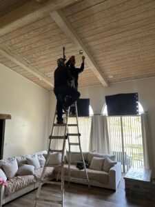 Two electricians on a ladder installing a ceiling fixture in a living room, performed by MCM Electrical Services LLC in Phoenix, AZ