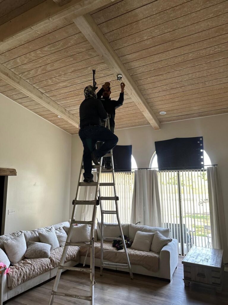 Two electricians on a ladder installing a ceiling fixture in a living room, performed by MCM Electrical Services LLC in Phoenix, AZ