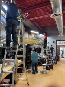 Multiple electricians on ladders installing ceiling fixtures and wiring in a commercial space for Flowers Electric in Aurora, CO.