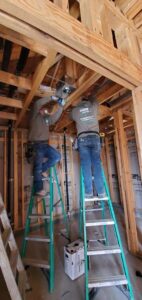 Two electricians from Shark Electric installing ceiling fixtures and wiring in a new construction home in Houston, TX.
