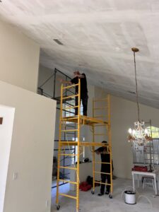 Two electricians on scaffolding installing ceiling wiring in a residential home by Krakkom Electric in Sunrise, FL.
