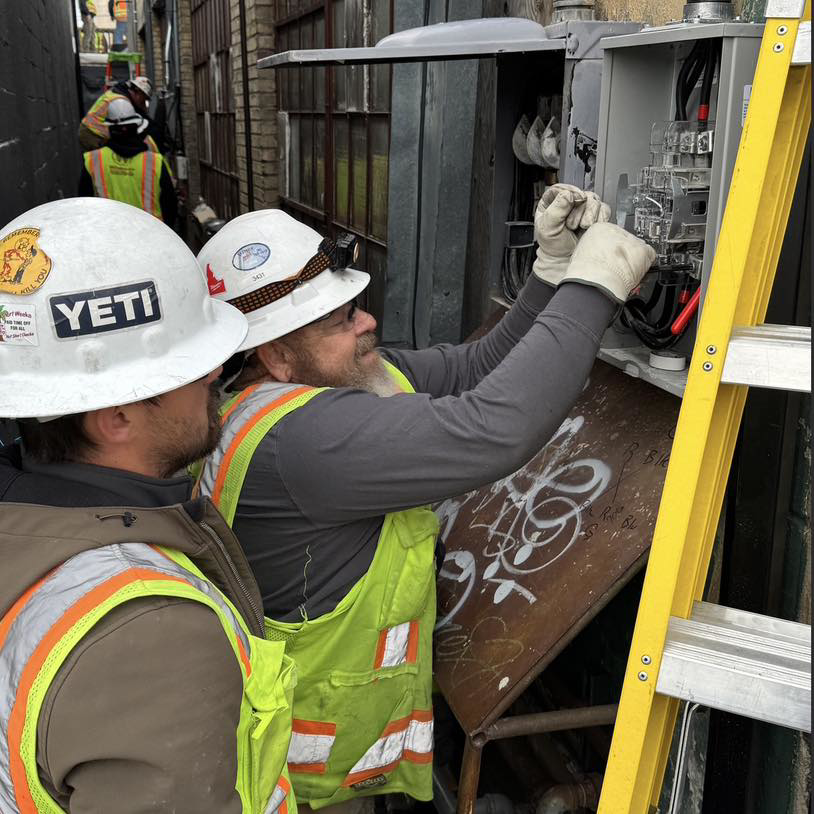Two electricians installing or repairing an outdoor electrical panel for Wheeler Electric, Inc. in Idaho Falls, ID.