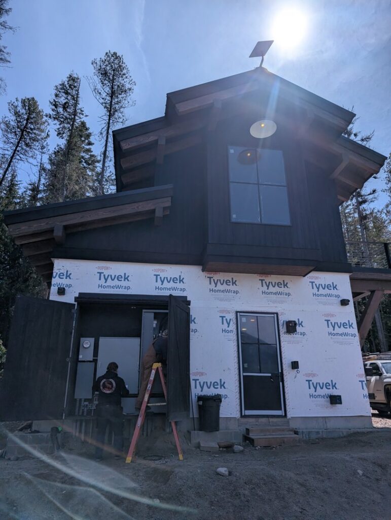 Two electricians installing electrical panels and wiring on the side of a house for Great Northern Power in Kalispell, MT.