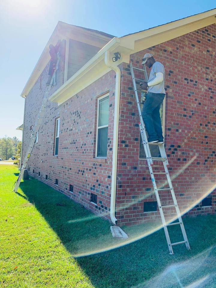 Two Gksquad electricians on ladders installing or repairing exterior electrical components on a brick house in Columbia, SC.