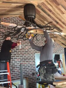 Two electricians installing a large, intricate chandelier for President, Cannizzo Electric, Inc. in Rochester, NY.