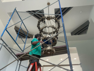Outlaw Electric electricians on scaffolding installing a large, ornate chandelier in a high-ceiling home in Tulsa, OK.