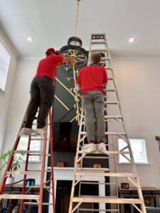 Two electricians from Revamp Athens Electrical Company installing a large, ornate chandelier in Athens, GA.