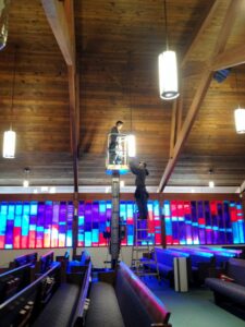 Two electricians from Obot Electric installing overhead lights in a large hall in Bellevue, WA.